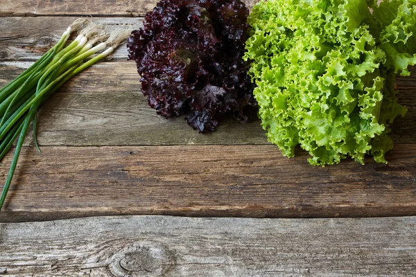 Eski pürüzlü ahşap yüzey, sağlıklı beslenme konsepti, seçici odak üzerinde kök ve genç soğan demet ile yeşil ve kırmızı taze marul