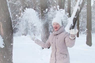 Karlı bir ormanda kış giysileri genç kadın beyaz kar atar ve gülüyor, seçici odak