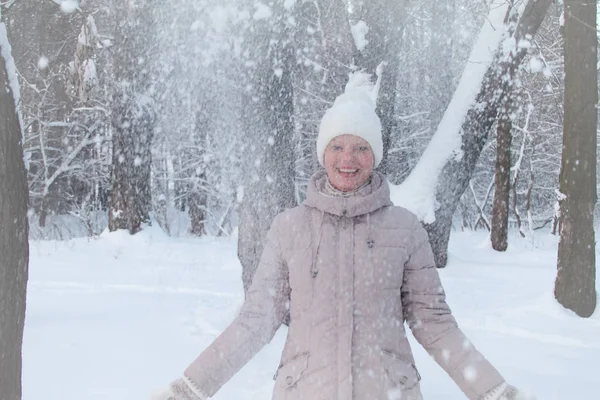 Young woman in winter clothes in a snowy forest throws white snow and laughs, selective focus