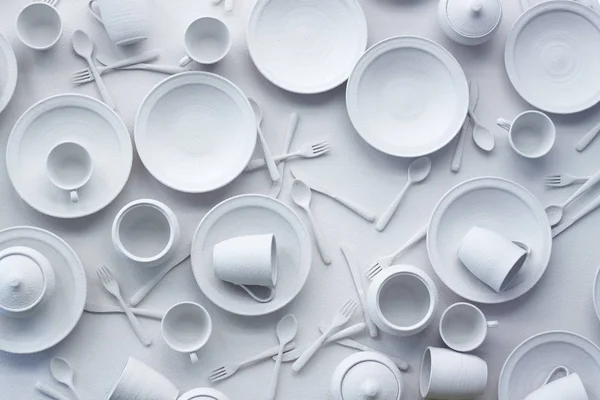 Многие блюда и приборы окрашены в белый цвет на белой поверхности, концепция чрезмерного потребления, избирательный фокус — стоковое фото