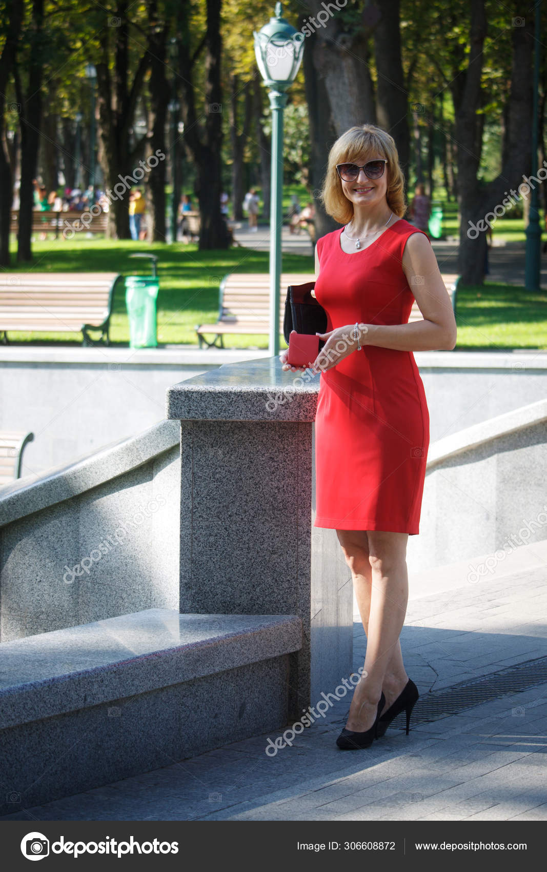 Mature middle-aged woman in red dress with a red gift box standing