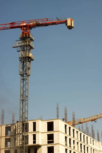Primer plano de la parte superior de una grúa torre roja cerca de un nuevo edificio contra un cielo azul, enfoque selectivo — Foto de Stock