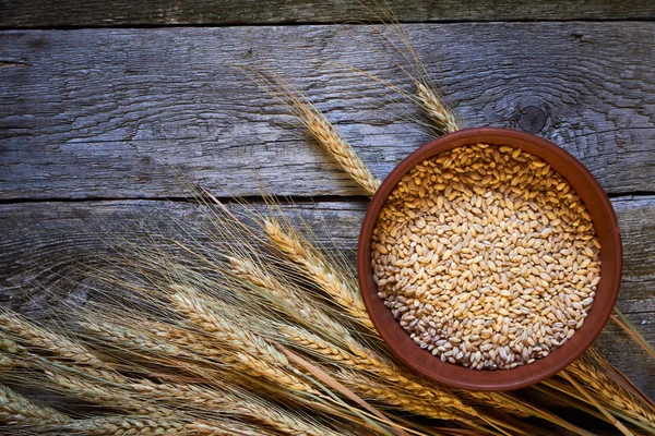 Orelhas de trigo e uma tigela de trigo em uma tábua de madeira escura, foco seletivo — Fotografia de Stock