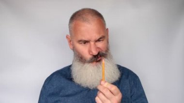 Olgun adam kalemini kalemle sivriltir. Komik sakallı büyükbaba suratını buruşturuyor. Gri arka planda üst düzey bir adamın portresi.