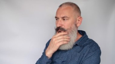 Düşüncelere dalmış çekici, orta yaşlı, beyaz bir adamın portresi. Gri arkaplan.