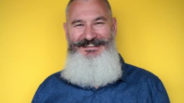 Sakallı, olgun bir adam onay veriyor. Gülümseyen yaşlı adam sarı arka planda baş parmak gösteriyor. İnsan jestleri ve duyguları.