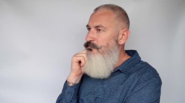 Çekici, orta yaşlı, beyaz sakallı, düşünceli ya da üzgün bir adamın portresi. Gri arkaplan.