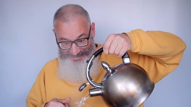 Hombre maduro barbudo alegre tonto vierte agua hirviendo de la tetera en la prensa francesa para hacer café. Buenos días concepto. Fondo gris . — Vídeos de Stock