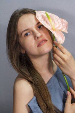 Gri arka planda pembe bir Anthurium çiçeği olan uzun saçlı esmer kızın şehvetli portresi.