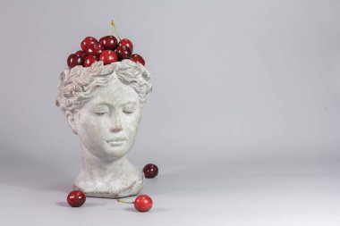 Kırmızı kirazlarla dolu Yunan tanrıçası şeklindeki şık dekorasyon. Güzel tasarım elemanları. Gri arkaplan.