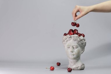 Kırmızı kirazlarla dolu Yunan tanrıçası şeklindeki şık dekorasyon. Güzel tasarım elemanları. Gri arkaplan.
