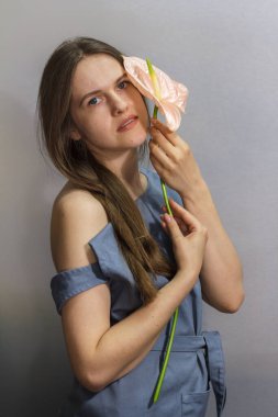 Gri arka planda pembe Anthurium çiçekli uzun saçlı esmer kızın şehvetli portresi.