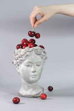 Kırmızı kirazlarla dolu Yunan tanrıçası şeklindeki şık dekorasyon. Güzel tasarım elemanları. Gri arkaplan.