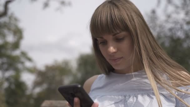 Дівчина з телефоном сидить на лавці — стокове відео