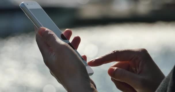 4k Une fille utilisant un smartphone au bord de la mer, surface de l'eau pétillante .