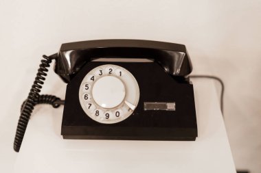 Klasik bir siyah döner telefon beyaz bir masanın üzerinde, 20. yüzyılın ortalarında parlak ve havadar bir uzay dizaynının eski cazibesini yakalıyor..