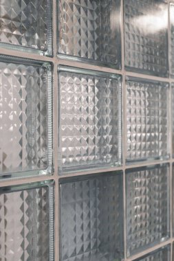 Yakından bakıldığında, doğal ışığı dağıtan, gün içinde çağdaş bir oda tasarımına derinlik ve zarafet katan desenli cam blok bir duvar görünür..