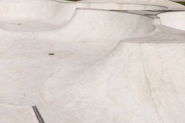 Pürüzsüz beton yapıda, gün ortası güneş ışığıyla aydınlatılan kaykay faaliyetleri için birbirine bağlı rampalar ve kaseler yer alıyor..