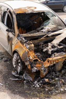 Bir araç, yanmış metal ve yanmış iç kısımlarda ciddi yangın hasarı gösteriyor. Olay bir şehir merkezinde meydana geldi. Talihsiz bir olaya işaret ediyor..
