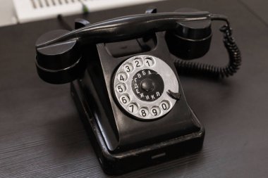 Koyu ahşap bir masada yuvarlak kadranlı klasik bir siyah döner telefon sergilenir. Bu antika eser 20. yüzyılın ortalarında estetik ve zanaatkarlık sergiliyor..