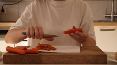 Parlak bir mutfak ortamında, bir kadın keskin bir bıçakla havuçları ustaca tıraş eder. Ellerine ve havuçlarına odaklanarak besleyici bir yemek hazırlıyor..