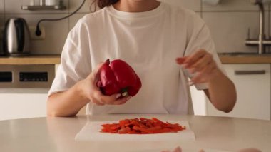 Bir kadın iyi donanımlı bir mutfakta ustalıkla taze kırmızı biber keser. Yakın çekim, yaklaşan yemek için gerekli malzemeleri hazırlarken tekniğini gösteriyor..