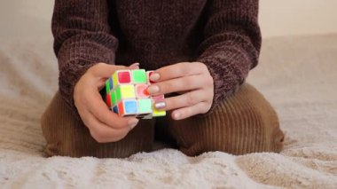 Chemnitz, Almanya - 06-09-2025: bir Rubiks küpünü çözmeye odaklanmış bir kadın oturma odasında rahatça oturuyor. Elleri onu tamamlamak için stratejiler geliştirirken renkli bulmacaları ustalıkla manipüle ediyor.