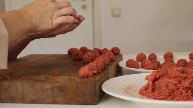 Bir kadın mutfakta özenle çalışıyor, lezzetli köfteler hazırlıyor. Geleneksel yemek pişirme yöntemleri ve taze malzemelerin altını çizerek karışımı ustalıkla mükemmel şekillere sokuyor..