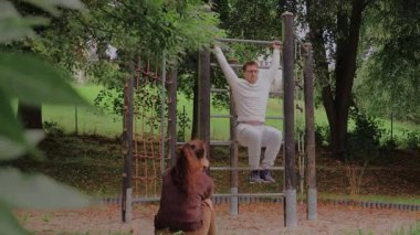 Bir çift parkta kaliteli zaman geçiriyor, kahkaha ve neşe paylaşıyorlar. Partnerlerden biri tırmanma iskeletinde sallanırken, diğeri aşağıdan izliyor, doğa tarafından çevrelenmiş..