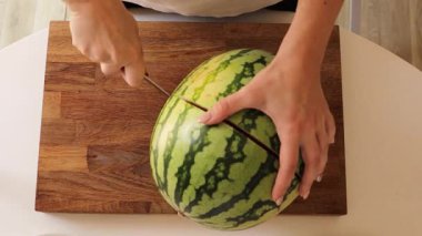 Parlak bir mutfakta, bir kadın büyük bir karpuzu ustalıkla üniforma parçalarına ayırır. Her kesik, canlandırıcı bir ziyafet hazırlamaktan zevk aldığı için sulu, canlı kırmızı iç mekanı gözler önüne seriyor..