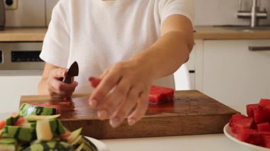 Bu yakın plan, karpuzu ustalıkla keserek düzgün, üniformalı parçalar haline getiren bir kadını yakalıyor. Mutfak parlak ve modern. Meyveyi keserken tekniğini ve hassasiyetini vurguluyor..