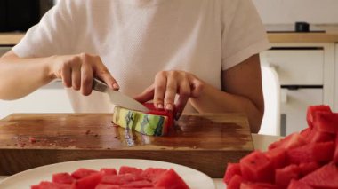Parlak bir mutfakta bir kadın, sağlıklı bir yaz atıştırması hazırlamak için taze karpuzu ustalıkla küçük parçalara ayırır. Süreç onun tekniğini ve sulu meyvelerin canlı rengini gösteriyor..