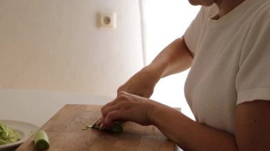 Tahta kesme tahtasına ustalıkla pırasa kesen bir kadının yakın çekimi. Basit mutfak düzenlemesi sağlıklı yemek pişirme ve yemek hazırlama üzerine odaklanmayı yansıtıyor..