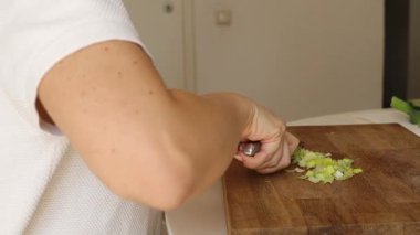 Ahşap kesme tahtasındaki pırasayı ustalıkla dilimleyen bir kadına yaklaş. Modern bir mutfakta taze malzemeler hazırlıyor. Önünde lezzetli bir yemek olmasını sağlıyor..