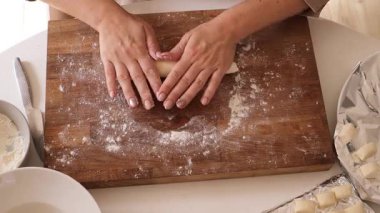 Bir kadın süzme peynir kullanarak körileri ustalıkla hazırlar, ahşap bir yüzeyde karışımı yoğururken ellerinin yakın planlarını gösterir. Un ve malzemeler düzgünce yerleştirilmiş..