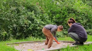 Genç bir anne, çocuğuyla doğal ortamında gezip oynarken kaliteli zaman geçirir. İkisi gülüyor ve kumda yemyeşil şekiller yaratmaktan zevk alıyorlar..