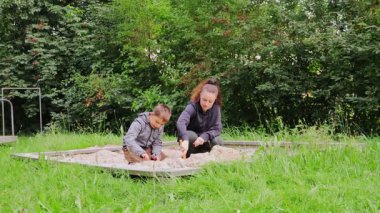Genç bir anne ya da dadı kum havuzunda bir çocukla iletişim kurar, doğanın yeşilliğiyle zenginleşen canlı bir oyun alanında yaratıcılığı ve neşeyi teşvik eder..