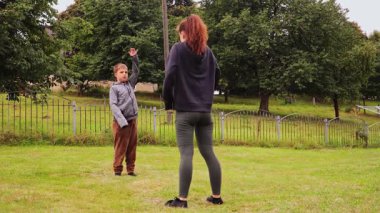 Canlı bir arka bahçe ortamında, genç bir kadın çocuğuyla spor egzersizleri yapıyor. Sağlıklı alışkanlıkları desteklerken aynı gülümsemeyi paylaşıyorlar..