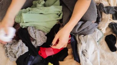 Rahat bir ortamda, genç bir kadın elbiselerini özenle katlıyor ve çamaşırlarını düzenliyor. Çeşitli kumaşları sınıflandırıyor, temiz çamaşır yığınları oluşturuyor..