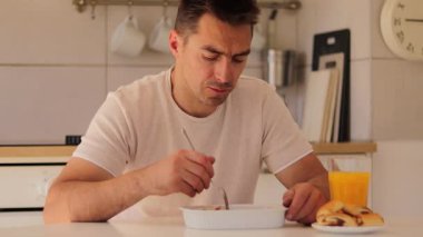 Sıcak bir mutfakta, bir adam masaya oturur ve bol bol lazanya yer. Portakal suyunu yudumlarken yemeğine odaklanıyor. Huzurlu bir öğle yemeği anının tadını çıkarıyor..