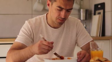 Rahat bir mutfak ortamında, bir adam elinde bir bardak portakal suyu tutarken bir tabak lazanyanın tadını çıkarıyor. Öğle yemeği sırasında ev yapımı yemekten hoşlanıyor gibi görünüyor..