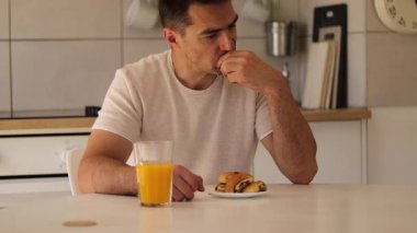 Bir adam mutfak masasında oturmuş portakal suyu içerken olgun bir armudun kıymetini biliyor. Kahvaltısının tadını çıkarmak için bir dakikasını ayırıyor, evde sağlıklı bir yaşam tarzını benimsiyor..