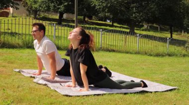 Bir çift, arka bahçelerindeki bir paspasın üzerinde yoga egzersizi yapıyor. Temiz havanın ve güneşin tadını çıkarırken bir yandan da bağlantılarını güçlendiren bir fitness rutinine girişiyor..