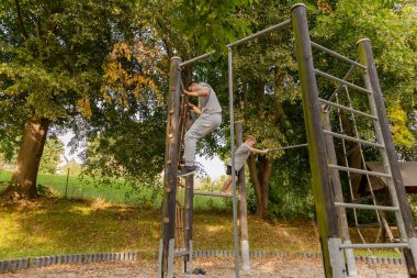Bir baba ve çocuğu, güneşli bir günde yemyeşil bir havayla çevrili iken, birlikte oyun alanında vakit geçiriyorlar, ekipmanların üzerine tırmanıyorlar..