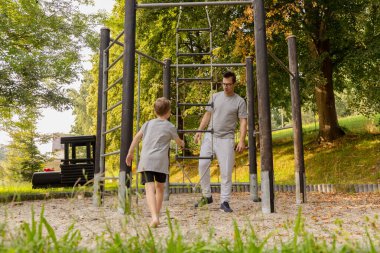 Bir baba ve küçük oğlu canlı yeşilliklerle çevrili bir oyun parkında neşeli bir oyun zamanı geçiriyorlar. Ekipmanları incelerken kahkahaları ve değerli anları paylaşıyorlar..