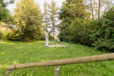 Bir baba çocuğuyla bir parkta, yemyeşil ağaçlar ve çimlerle çevrili olarak oynar. Açık havada eğlenirken kahkaha ve neşeyi paylaşırlar..