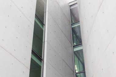 Eşsiz bir bina tasarımı düz beton duvarlar ve büyük cam pencereler içerir. Yapı, şehir ortamında modern mimari teknikleri vurguluyor..