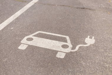 Açık bir şekilde tanımlanmış elektrikli araç şarj noktası, şehrin asfalt park alanına, basit bir araba taslağı ve bir elektrik prizi sembolü ile boyanmıştır..