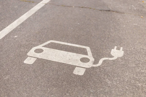 Açık bir şekilde tanımlanmış elektrikli araç şarj noktası, şehrin asfalt park alanına, basit bir araba taslağı ve bir elektrik prizi sembolü ile boyanmıştır..