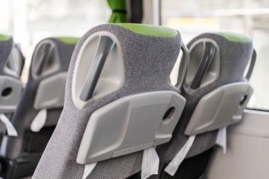 Otobüsün içinde, modern koltuklar rahat ve stil için tasarlanmış, yumuşak gri kumaş ve canlı yeşil detaylar içeriyor. Her koltuk arkasında düşünceli tasarım unsurları sergiliyor..
